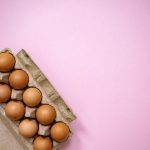 Brown eggs arranged in a carton on a pastel pink background, highlighting organic and fresh produce.