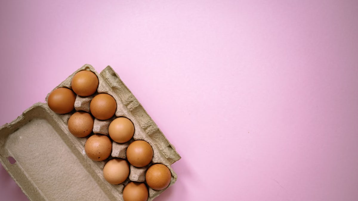 Brown eggs arranged in a carton on a pastel pink background, highlighting organic and fresh produce.